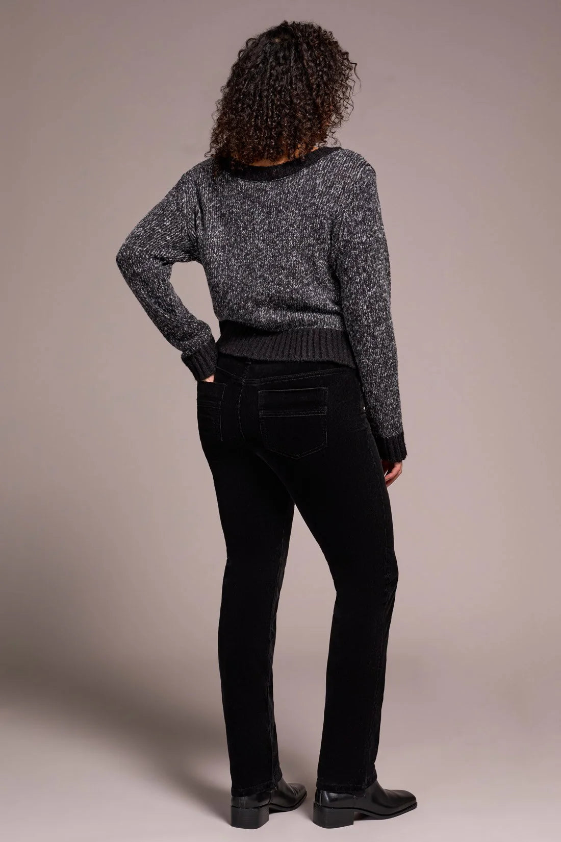 Person wearing a gray knitted sweater and black pants against a beige background