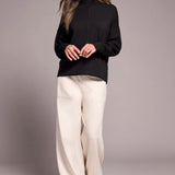Woman wearing a black turtleneck and white pants against a gray background