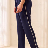 A person wearing navy blue athletic pants with a cream-colored side stripe, paired with beige sneakers, standing in a brightly lit indoor setting.