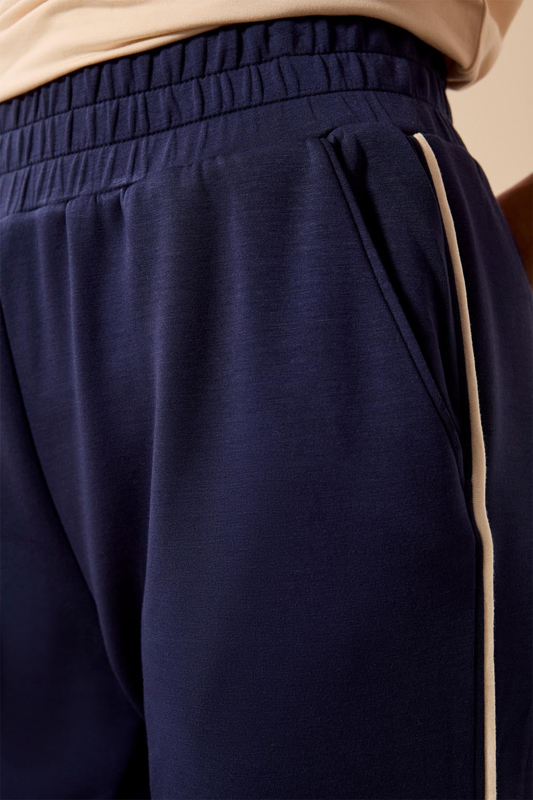 Close-up of navy blue athletic pants with a beige side stripe and a beige waistband, worn with a beige top.