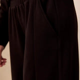 Close-up of a person wearing dark brown wide-leg lounge pants with an elastic waistband and side pockets.