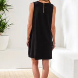 Woman wearing a black sleeveless dress in a minimal indoor setting