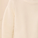 Close-up of a cream ribbed turtleneck sweater worn by a model, showing the fine horizontal ribbed texture of the knit fabric.