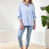 Woman wearing a light blue shirt and jeans standing in a room with a plant.