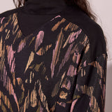 Close-up of a person wearing a black sweater with abstract multicolor pattern.