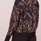 A woman shown from the back wearing a top with a gold and pink abstract leaf pattern, paired with black pants.