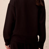 Person wearing a black outfit against a beige wall