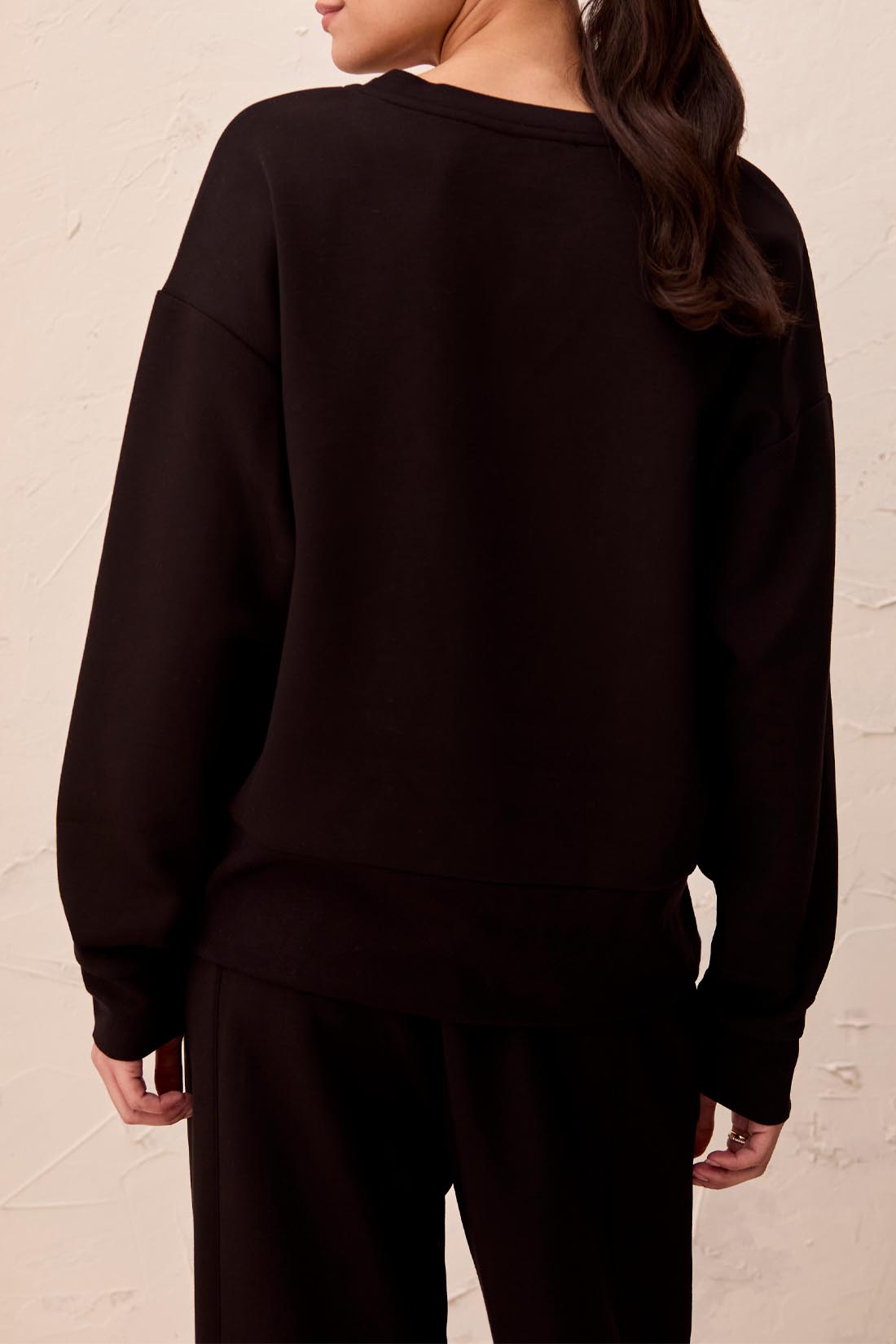 Person wearing a black outfit against a beige wall