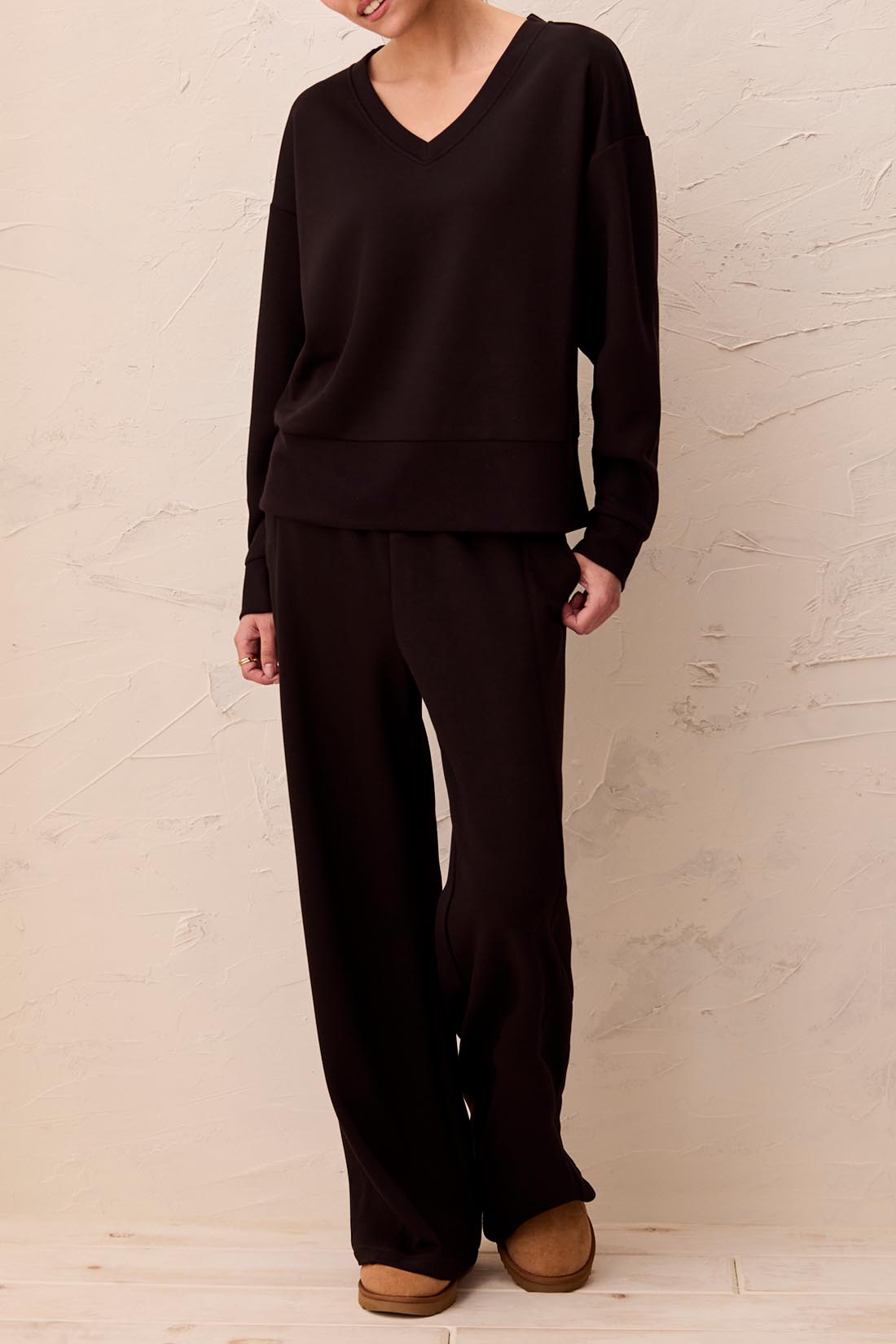 Person wearing a black outfit against a beige wall