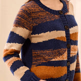 A woman wearing a chunky knit cardigan sweater with horizontal stripes in navy blue, rust orange, and cream, featuring dark brown buttons down the front.