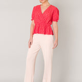 This stretchy wrap blouse in a coral colour has an elastic waist with a small ruffle underneath. The puff sleeves are short and have an elastic cuff.