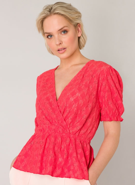 This stretchy wrap blouse in a coral colour has an elastic waist with a small ruffle underneath. The puff sleeves are short and have an elastic cuff.
